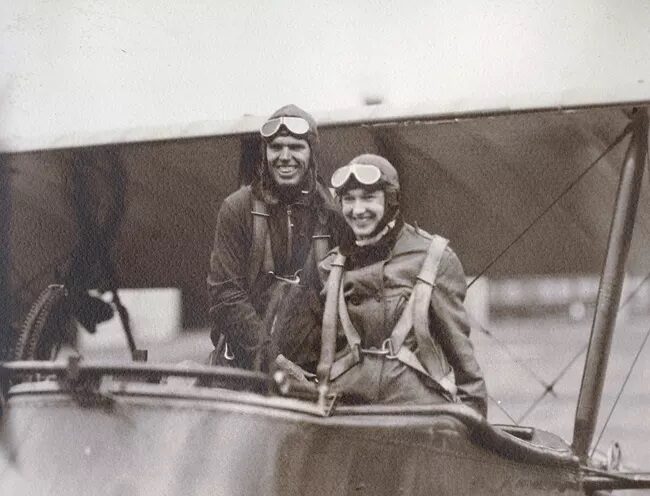 Black and white photo of two smiling aviators in the open cockpit of an old fashioned plane